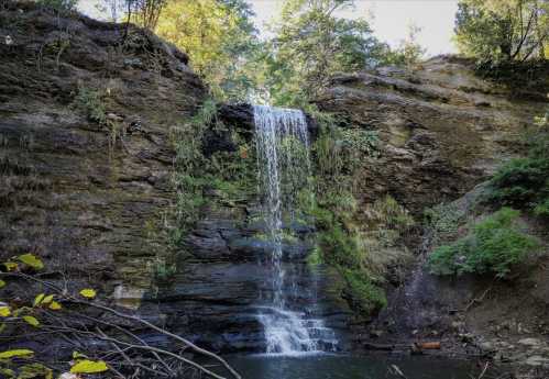 A serene waterfall cascading down rocky cliffs, surrounded by lush greenery and a tranquil pool below.