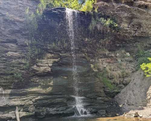 A serene waterfall cascading down rocky cliffs, surrounded by lush greenery and a calm pool below.