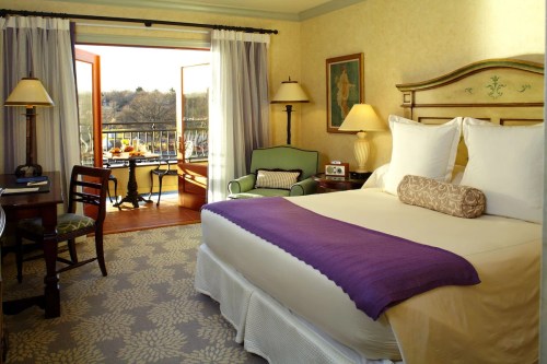 Cozy hotel room with a king bed, purple throw, desk, and balcony overlooking a scenic view.