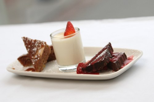 A dessert plate featuring a glass of panna cotta, chocolate cake slices, and a piece of honeycomb, garnished with a strawberry.