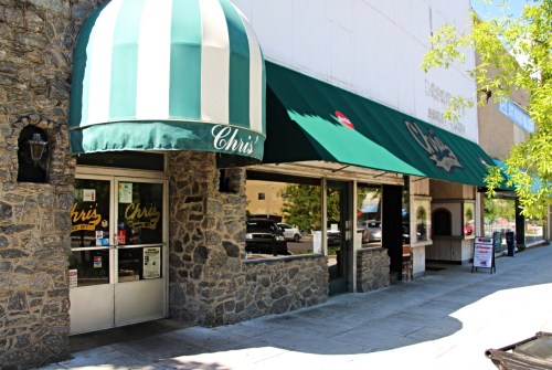 Exterior of Chris's restaurant featuring a green and white striped awning and stone facade, with outdoor seating visible.