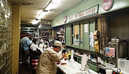 A bustling diner with patrons at the counter, enjoying food and drinks in a cozy, retro setting.