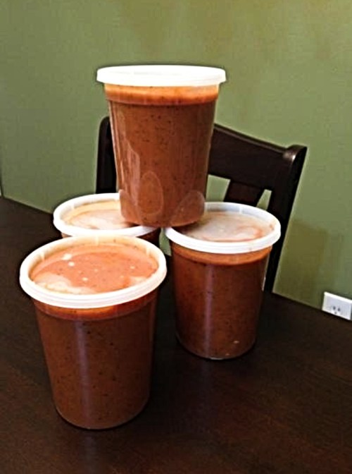 Four containers of brown sauce stacked on a table against a green wall.