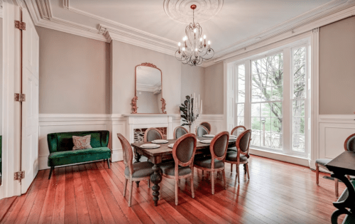 Elegant dining room with a wooden table, upholstered chairs, a green velvet sofa, and large windows.