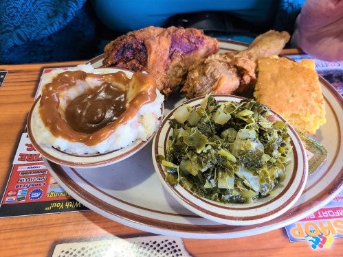 A plate of fried chicken, cornbread, collard greens, and mashed potatoes with gravy.