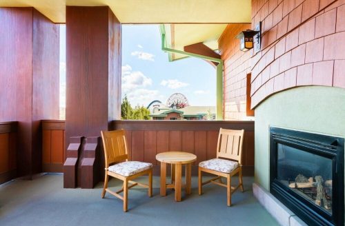 A cozy balcony with two wooden chairs and a small table, overlooking a scenic view with a ferris wheel in the background.