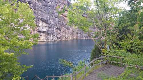 A serene lake surrounded by rocky cliffs and lush greenery, with a wooden pathway leading to the water's edge.