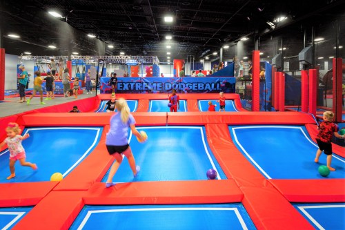 Children playing extreme dodgeball on trampolines in a vibrant indoor arena. Bright colors and active atmosphere.