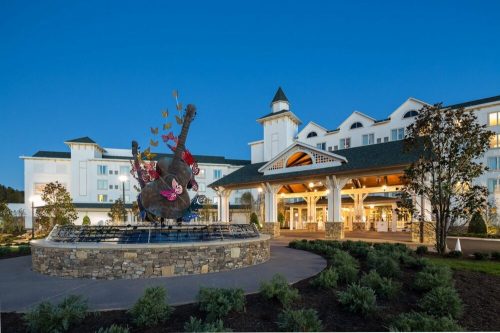 A hotel entrance featuring a large guitar sculpture surrounded by butterflies, with a landscaped area and evening sky.