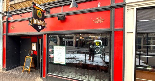 A Guinness sign hangs in the window below the shamrock sign at the red exterior of Donnelly's Pub in Iowa City.