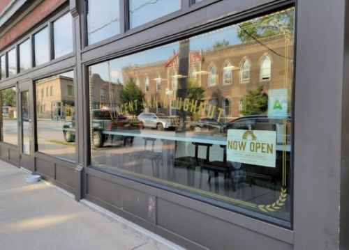 A storefront with large windows displaying a "NOW OPEN" sign and a view of the street outside.