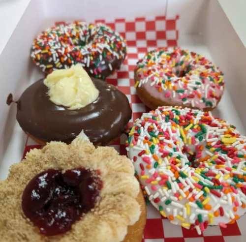 A box of assorted donuts: chocolate, sprinkles, and a jelly-filled donut with cream on top.