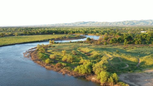 Aerial view of a winding river surrounded by lush greenery and rolling hills in the background.
