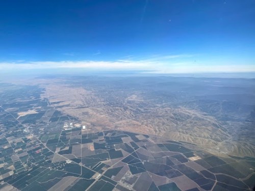 Aerial view of vast agricultural fields and rolling hills under a clear blue sky.
