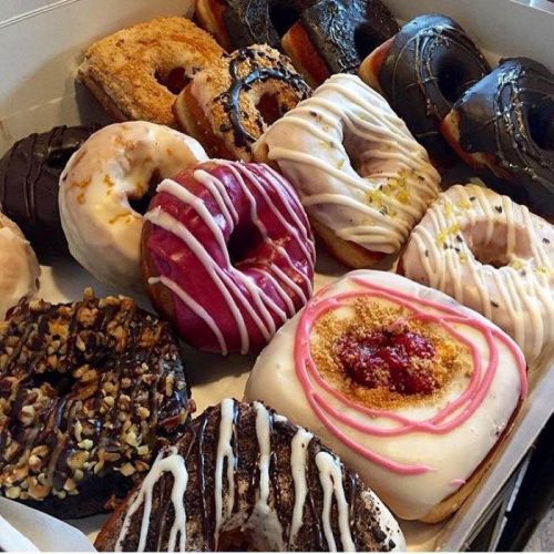 A variety of colorful donuts with different toppings and glazes arranged in a box.