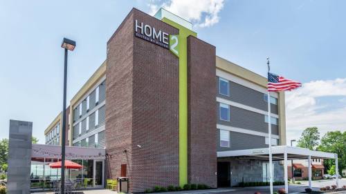 Exterior view of a Home2 Suites hotel with a brick facade, green accents, and an American flag in front.