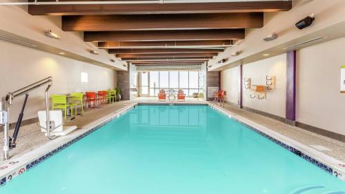 Indoor swimming pool with turquoise water, surrounded by colorful chairs and large windows letting in natural light.