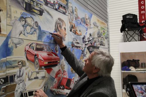 An artist paints a mural featuring classic cars and racing scenes, capturing a nostalgic automotive theme.