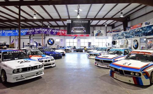 A collection of classic BMW race cars displayed in a spacious automotive museum.