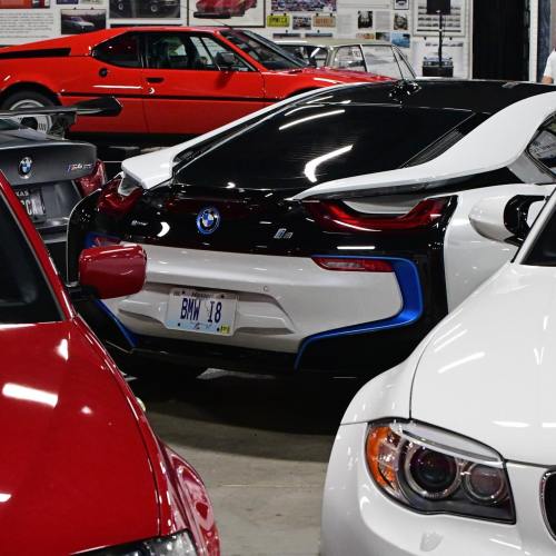 A BMW i8 parked among various classic and modern cars in a garage setting.