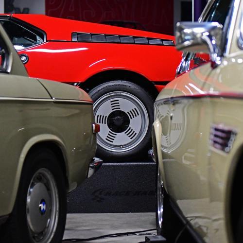 A red sports car is flanked by two vintage cars in a garage, highlighting their classic designs.