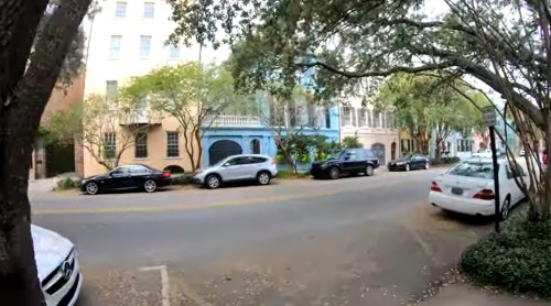 A street lined with trees and parked cars, featuring colorful buildings in the background.