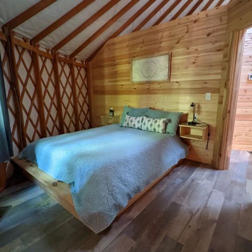 Cozy wooden bedroom with a queen bed, decorative pillows, and a warm, rustic atmosphere.