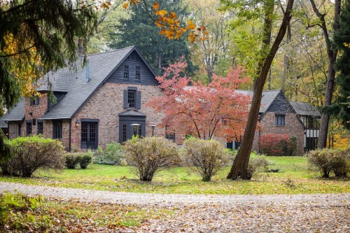 A charming brick house surrounded by colorful autumn trees and shrubs in a serene, wooded setting.
