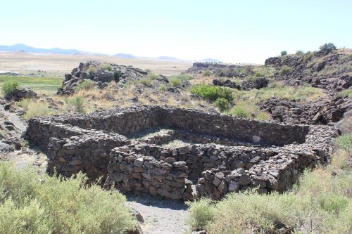 Ruins of a stone structure surrounded by sparse vegetation and hills under a clear blue sky.