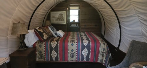 Cozy interior of a glamping tent featuring a bed with a patterned blanket and rustic decor.