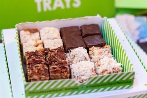 A box of assorted desserts featuring brownies, coconut bars, and nutty treats, arranged in neat rows.