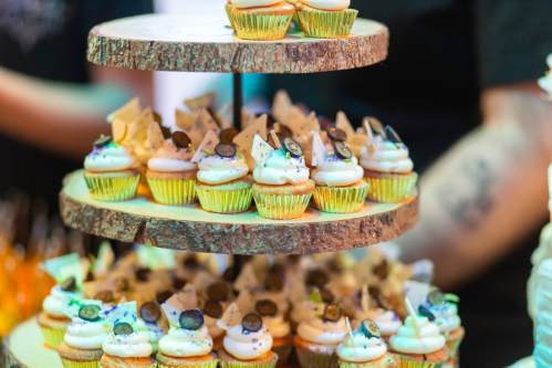 A tiered wooden stand displaying colorful cupcakes topped with frosting and decorative pieces.