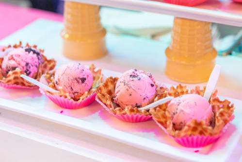 Four scoops of pink ice cream in waffle bowls, displayed on a white tray with small spoons.