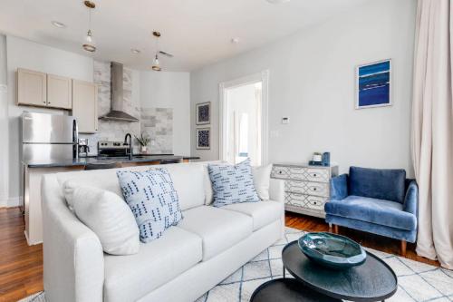 Cozy living room with a light sofa, blue armchair, coffee table, and modern kitchen in the background. Bright and inviting space.