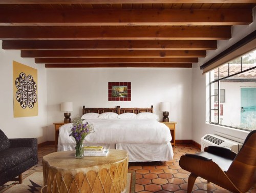 Cozy bedroom with a wooden bed, decorative art, a round coffee table, and large windows letting in natural light.