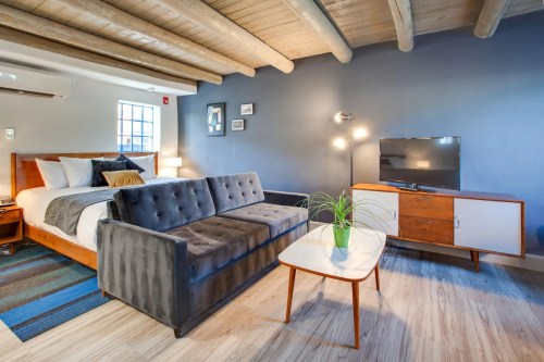 Cozy hotel room featuring a bed, sofa, TV, and modern decor with wooden beams and a small plant on the table.