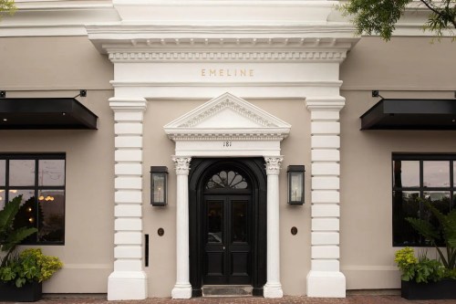 Exterior of a building featuring a grand entrance with a black door, white columns, and the name "Emeline" above.