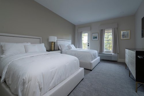 A modern hotel room with two beds, a dresser, and a window with natural light. Neutral color scheme.