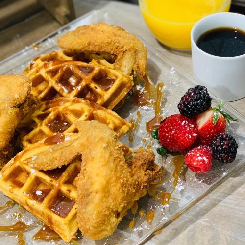 A plate of waffles topped with fried chicken, drizzled with syrup, alongside fresh berries and a cup of coffee.