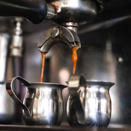 Close-up of espresso pouring from a machine into two stainless steel cups.