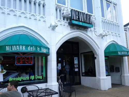 Exterior of Newark Deli & Bagels, featuring a bright "OPEN" sign and outdoor seating.
