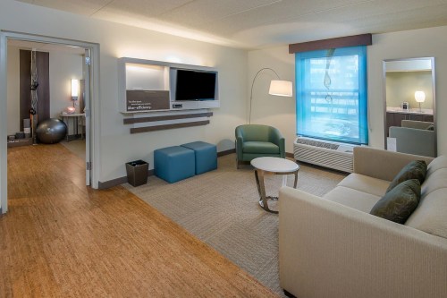 A modern hotel room featuring a seating area, TV, and exercise space with a ball and equipment. Bright and inviting decor.