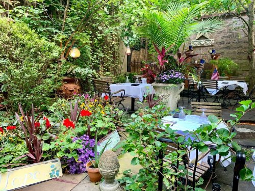 A lush garden patio with tables, colorful flowers, and greenery, creating a serene dining atmosphere.