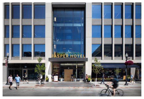 Modern building facade of Jasper Hotel with large windows, people walking, and bicycles in front.