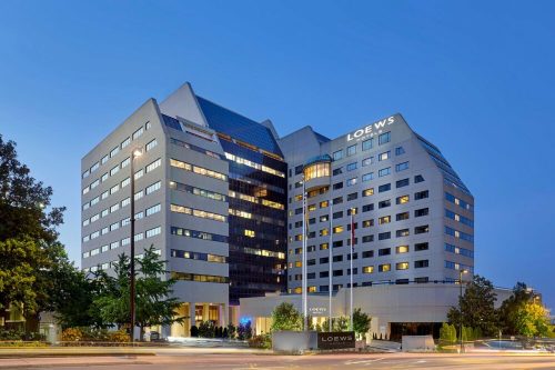 Modern hotel building at dusk, featuring large windows and a sleek design, with the name "Loews" prominently displayed.