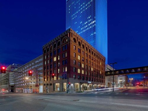 A historic brick building at night, with a modern skyscraper behind it, illuminated against a dark blue sky.