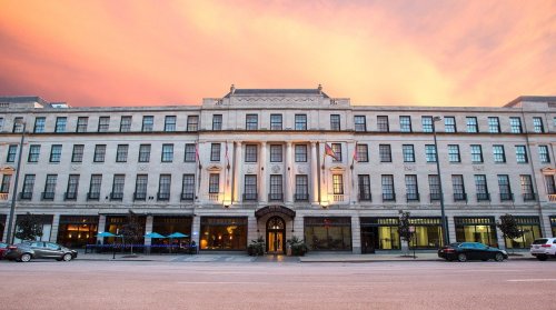 Historic building with a grand facade, illuminated at sunset, featuring flags and outdoor seating.
