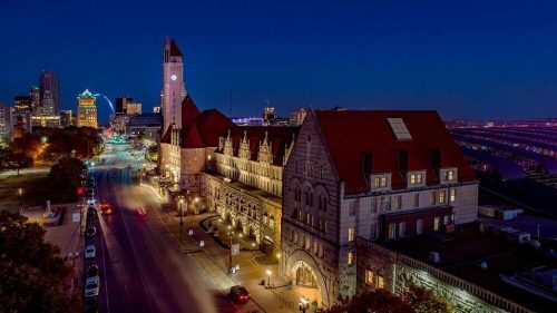 A cityscape at night featuring a historic building with a clock tower, illuminated streets, and a skyline in the background.