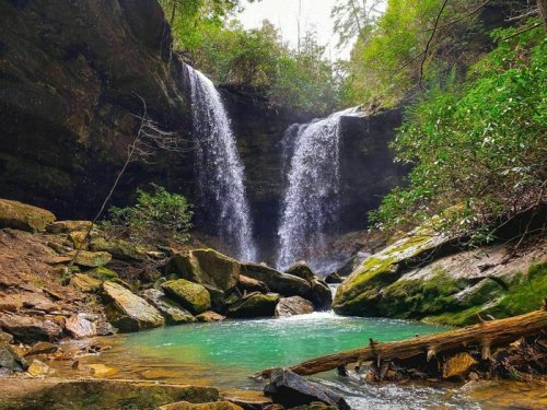 A serene waterfall cascades into a turquoise pool, surrounded by lush greenery and rocky terrain.