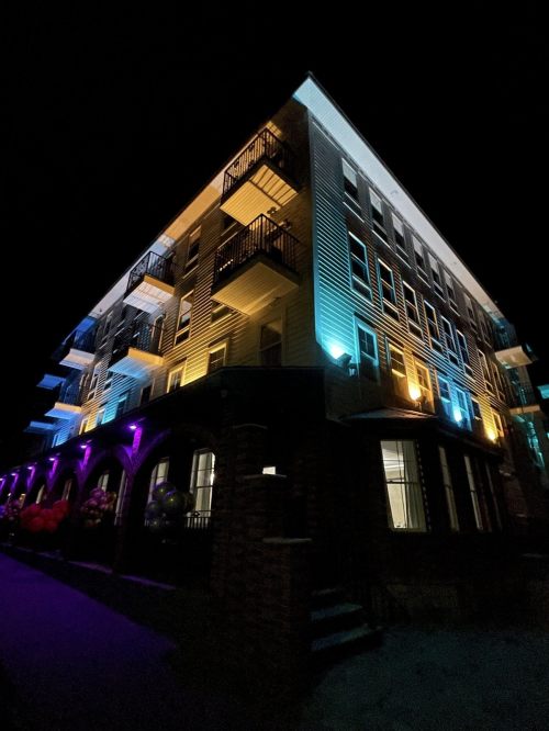 A modern building at night, illuminated with colorful lights and featuring balconies and a welcoming entrance.